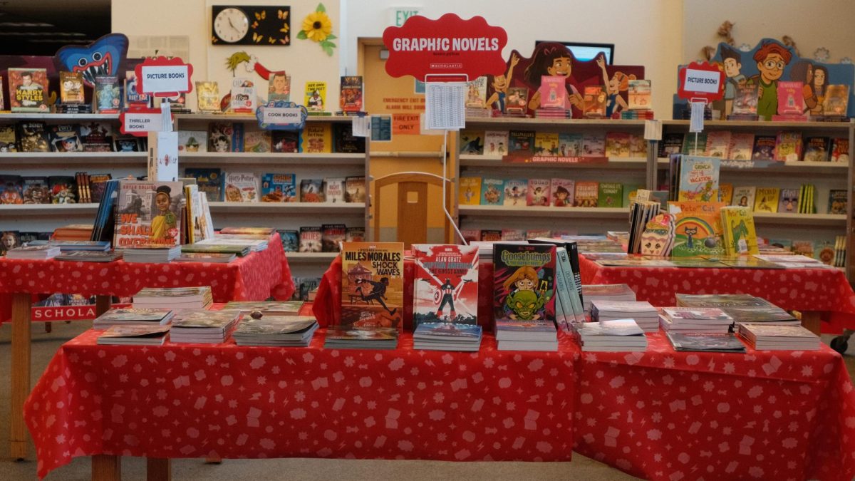 The book fair consisted of various tables with picture books and graphic novels surrounded by shelves that held novels and other titles.